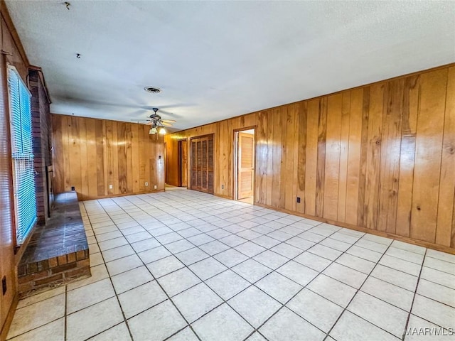 tiled empty room featuring ceiling fan and wood walls