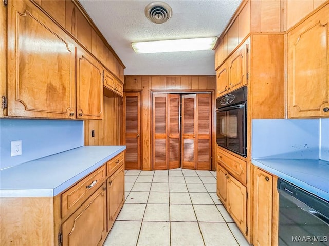 kitchen featuring light tile patterned floors, black appliances, a textured ceiling, and wood walls