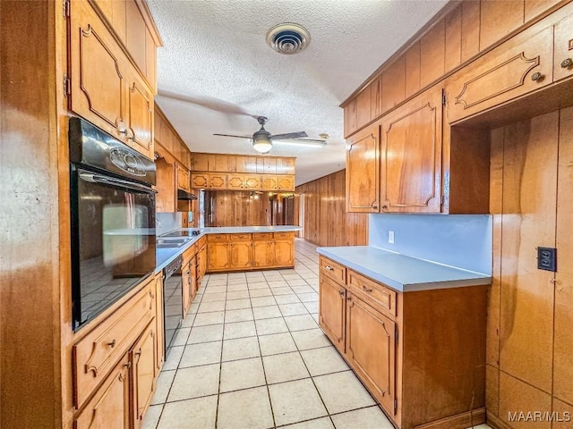 kitchen with ceiling fan, black appliances, a textured ceiling, light tile patterned flooring, and wood walls