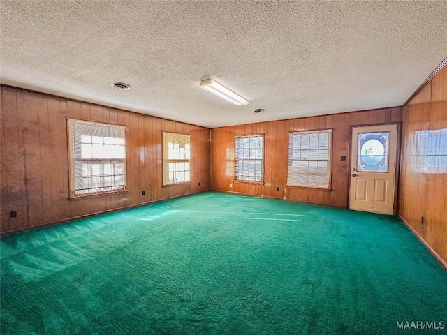 spare room featuring carpet floors, a textured ceiling, and wood walls