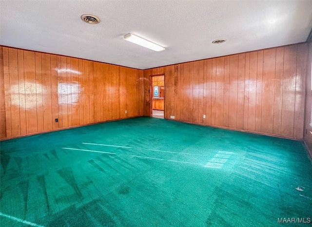 carpeted spare room with a textured ceiling and wood walls