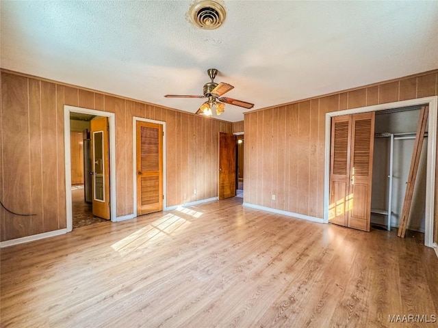 unfurnished bedroom featuring ensuite bathroom, light hardwood / wood-style flooring, a textured ceiling, multiple closets, and ceiling fan