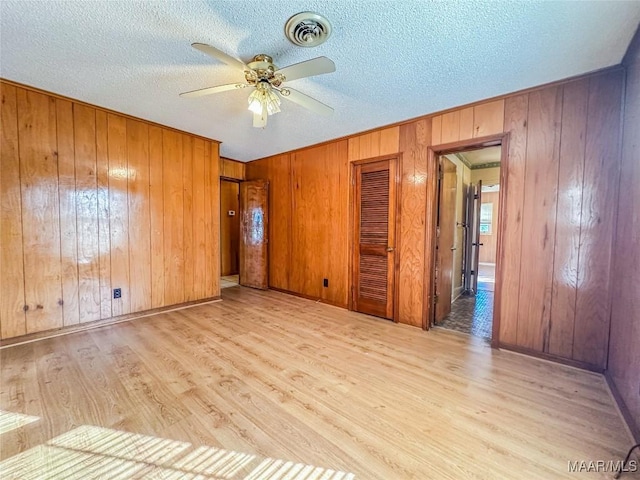 unfurnished room with a textured ceiling, wooden walls, ceiling fan, and light wood-type flooring