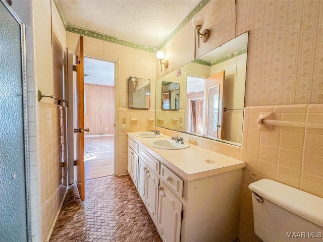 bathroom featuring tile walls, vanity, toilet, and a textured ceiling