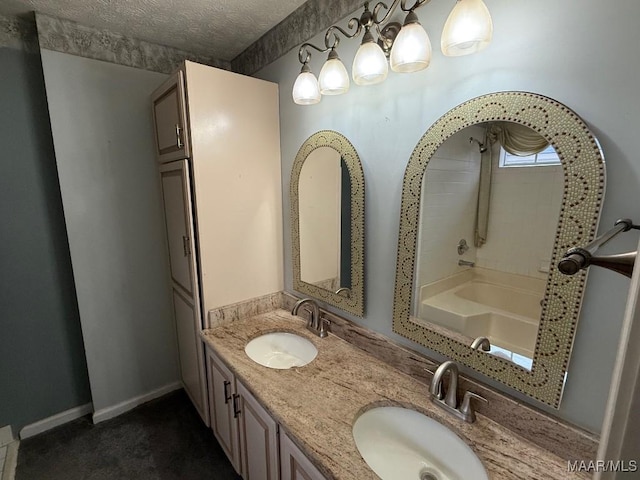 bathroom featuring a textured ceiling, double vanity, a sink, and baseboards