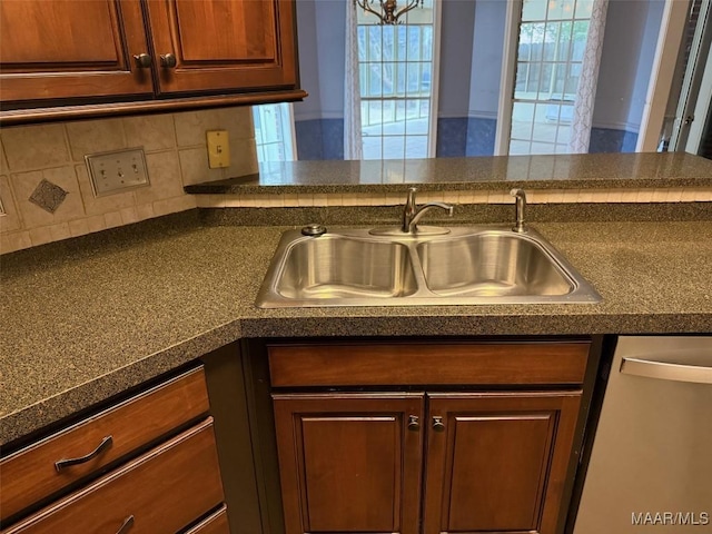 kitchen featuring dark countertops, stainless steel dishwasher, decorative backsplash, and a sink