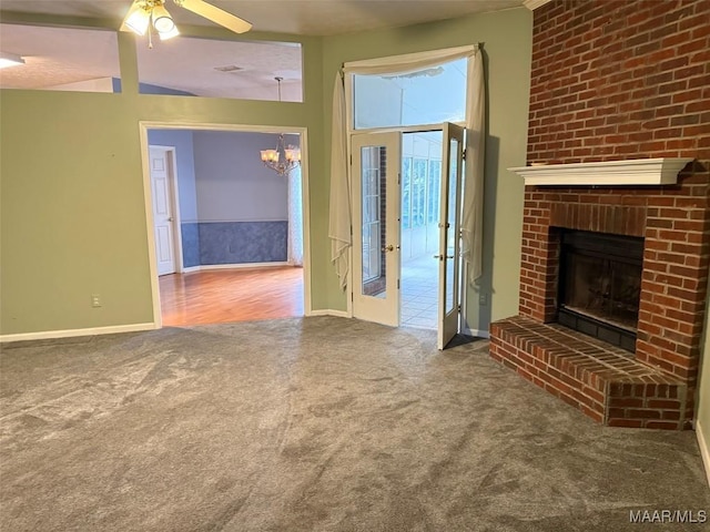 unfurnished living room featuring a brick fireplace, ceiling fan with notable chandelier, baseboards, and carpet floors