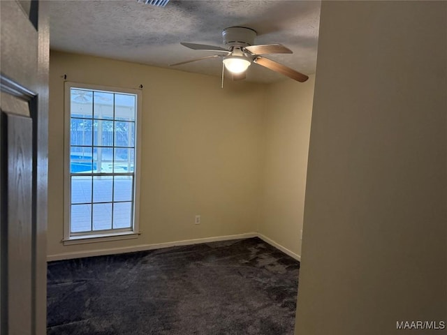 unfurnished room featuring a textured ceiling, dark carpet, a wealth of natural light, and baseboards