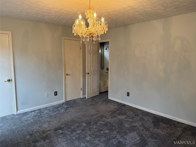 empty room featuring a textured ceiling, dark colored carpet, a notable chandelier, and baseboards