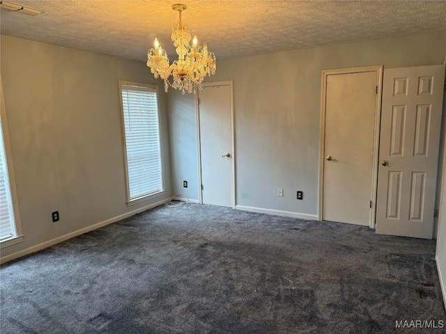 carpeted spare room featuring a notable chandelier, visible vents, baseboards, and a textured ceiling