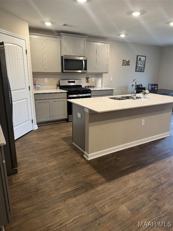 kitchen with appliances with stainless steel finishes, sink, a kitchen island with sink, and gray cabinetry