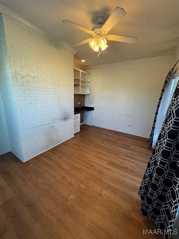 spare room featuring built in desk, dark hardwood / wood-style floors, ceiling fan, and brick wall