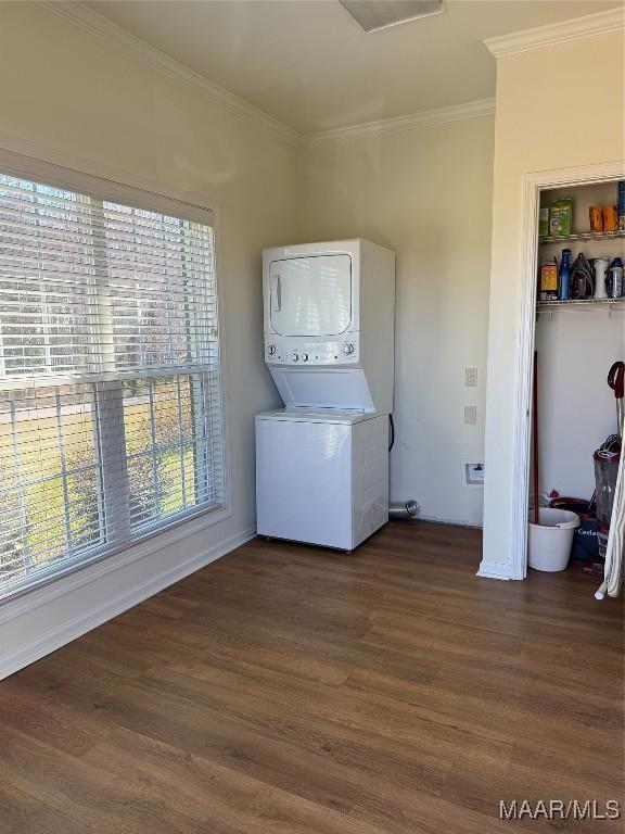 laundry room featuring crown molding, stacked washer / drying machine, and dark wood-type flooring