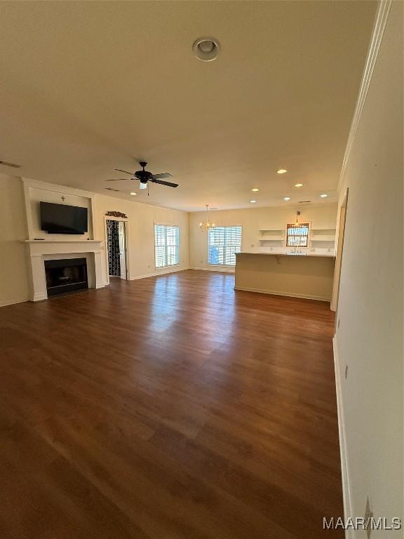 unfurnished living room featuring crown molding, ceiling fan with notable chandelier, and hardwood / wood-style flooring