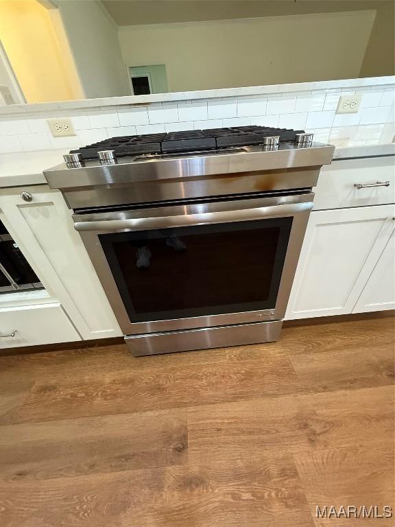 room details featuring tasteful backsplash, stainless steel gas range oven, white cabinets, and light hardwood / wood-style floors