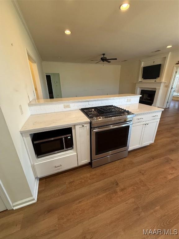 kitchen with stainless steel gas range, dark hardwood / wood-style floors, kitchen peninsula, ceiling fan, and white cabinets