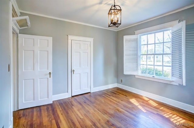 unfurnished bedroom featuring hardwood / wood-style floors, ornamental molding, a closet, and a chandelier