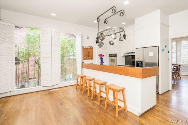 kitchen featuring light wood finished floors, white cabinets, a peninsula, stainless steel appliances, and a kitchen bar