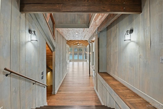 corridor featuring wooden walls, beam ceiling, and light hardwood / wood-style flooring