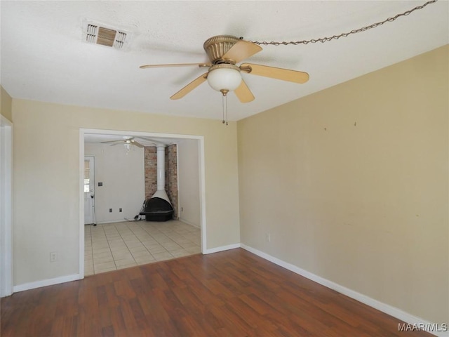 spare room featuring ceiling fan, a wood stove, and light hardwood / wood-style floors