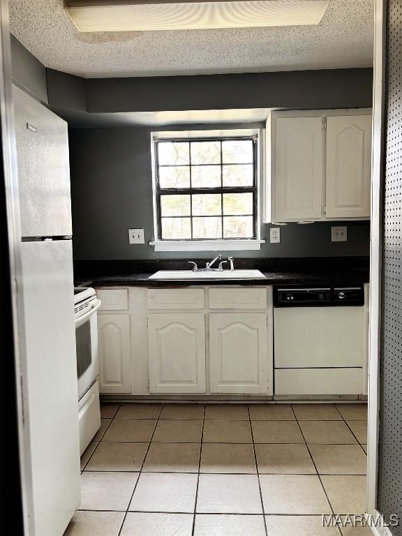 kitchen featuring white cabinetry, sink, light tile patterned floors, white appliances, and a textured ceiling