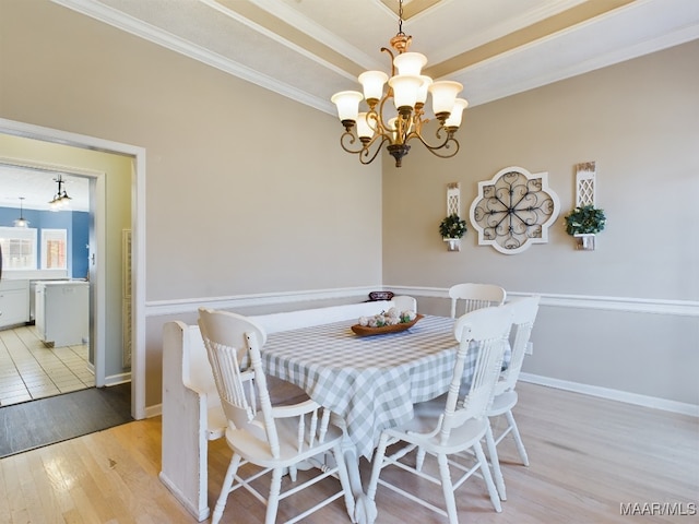 dining space featuring ornamental molding, an inviting chandelier, light hardwood / wood-style floors, and a tray ceiling