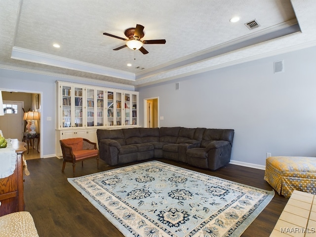 living room with a textured ceiling, ornamental molding, a tray ceiling, dark hardwood / wood-style flooring, and ceiling fan