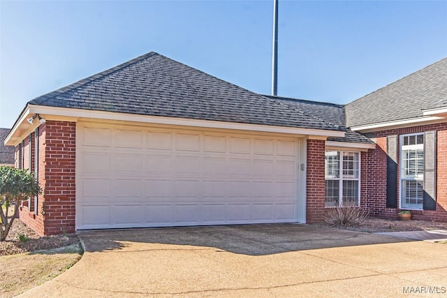 view of side of property with a garage, driveway, brick siding, and a shingled roof