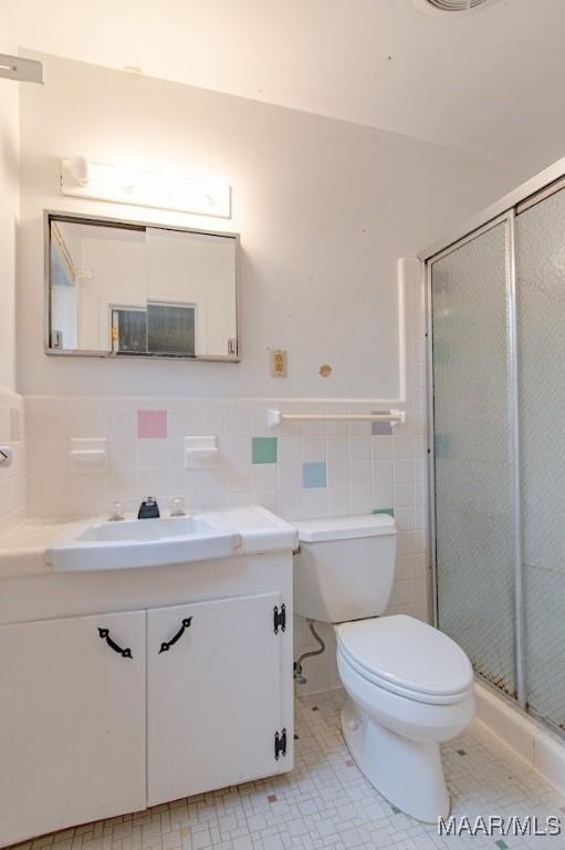 bathroom featuring tile walls, toilet, vanity, and a shower with shower door