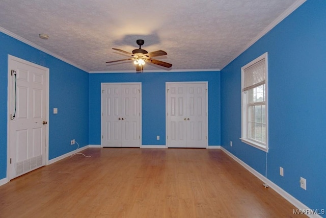 unfurnished bedroom with a textured ceiling, wood-type flooring, ornamental molding, and two closets