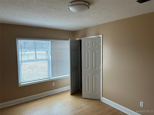 unfurnished bedroom with multiple windows, light hardwood / wood-style flooring, a closet, and a textured ceiling