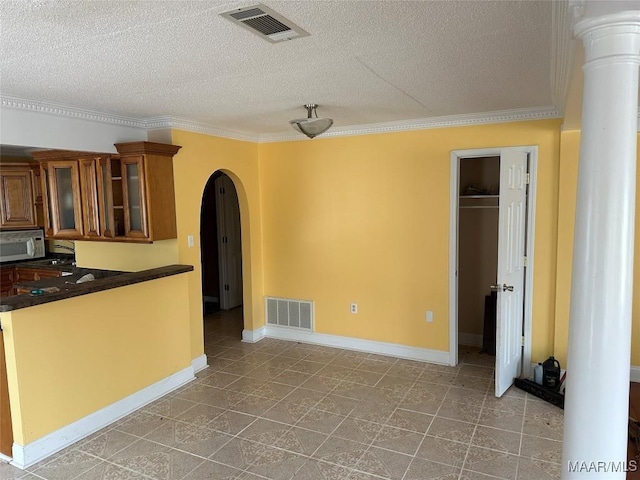 kitchen featuring ornate columns, crown molding, and a textured ceiling