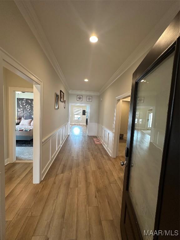 corridor with ornamental molding, wainscoting, a decorative wall, and wood finished floors