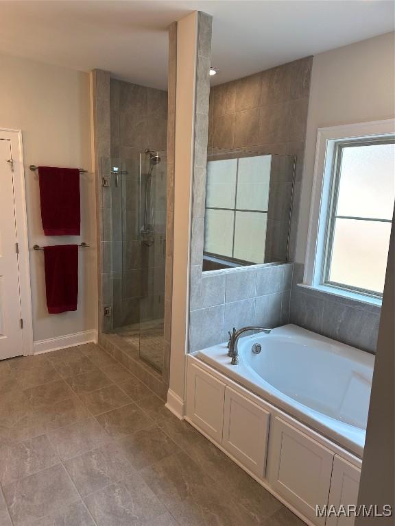 full bathroom with a garden tub, a shower stall, and baseboards