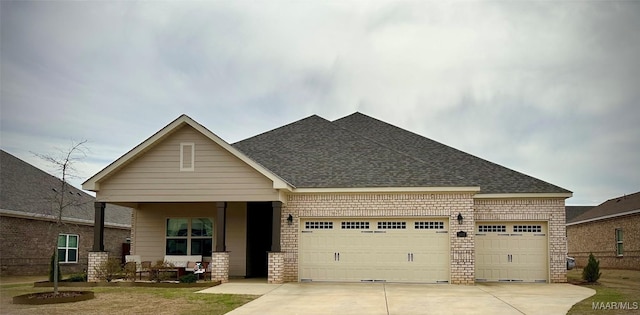 craftsman inspired home featuring a garage, driveway, brick siding, and a shingled roof