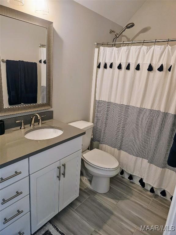 bathroom featuring toilet, lofted ceiling, a shower with shower curtain, and vanity