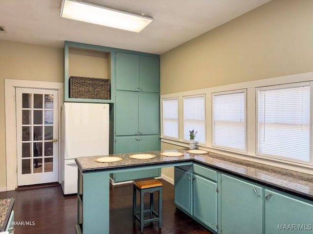 kitchen featuring green cabinetry, white fridge, a breakfast bar, and dark hardwood / wood-style flooring