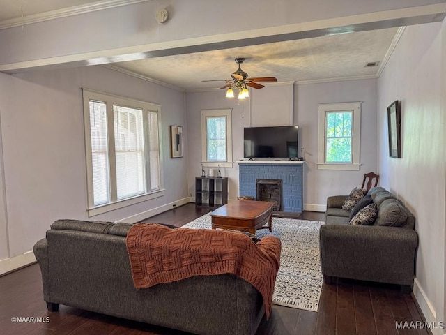 living room with dark wood-type flooring, a brick fireplace, crown molding, and ceiling fan