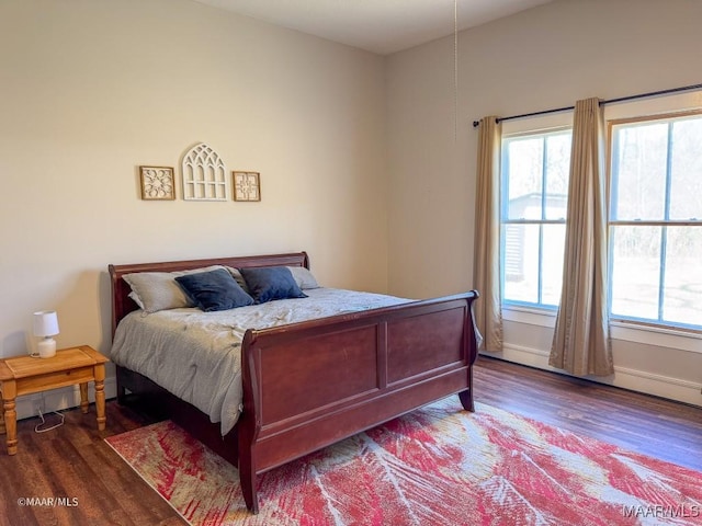 bedroom with baseboard heating, dark hardwood / wood-style floors, and multiple windows