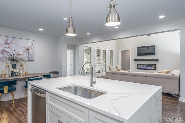 kitchen with sink, stainless steel dishwasher, hanging light fixtures, light stone countertops, and a kitchen island with sink