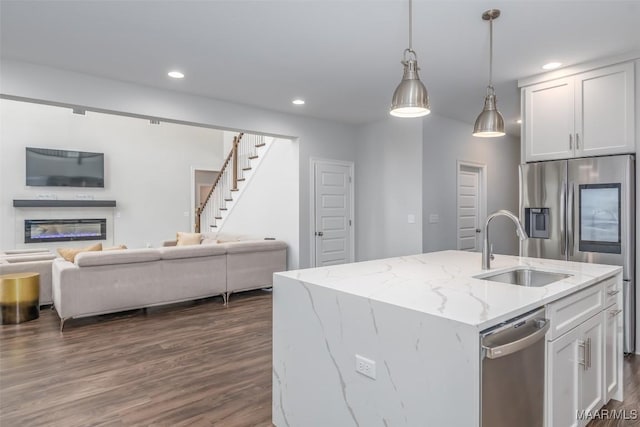 kitchen featuring an island with sink, white cabinets, light stone counters, and decorative light fixtures