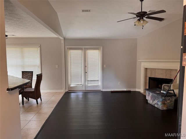 unfurnished living room featuring a healthy amount of sunlight, vaulted ceiling, french doors, and a tiled fireplace