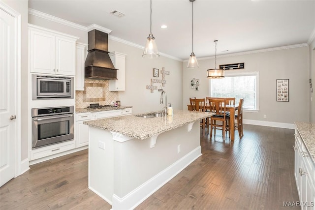 kitchen with appliances with stainless steel finishes, sink, custom exhaust hood, white cabinets, and an island with sink