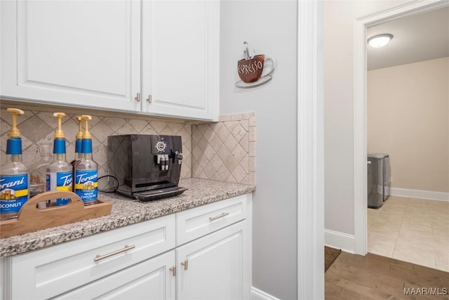 kitchen with light stone countertops, white cabinets, backsplash, dark tile patterned floors, and separate washer and dryer