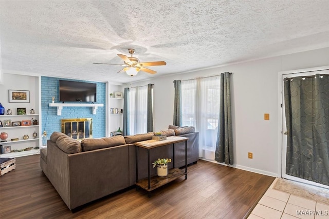 living room with ceiling fan, wood-type flooring, a textured ceiling, and a fireplace