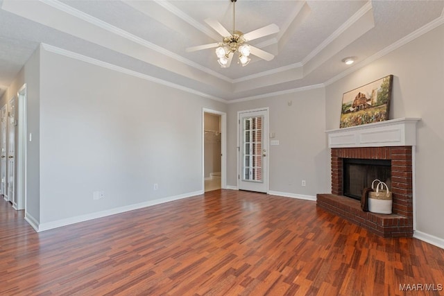 unfurnished living room with a brick fireplace, crown molding, a tray ceiling, and dark hardwood / wood-style floors