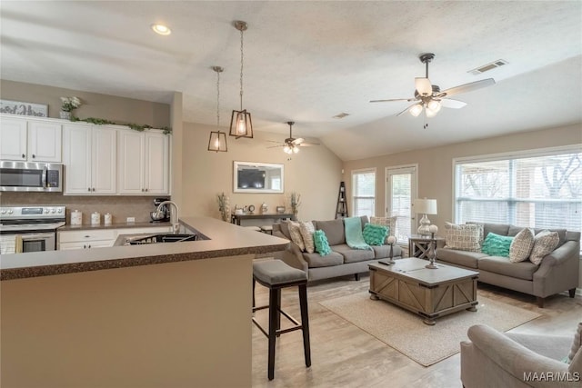 living room featuring light wood-type flooring, vaulted ceiling, sink, and ceiling fan