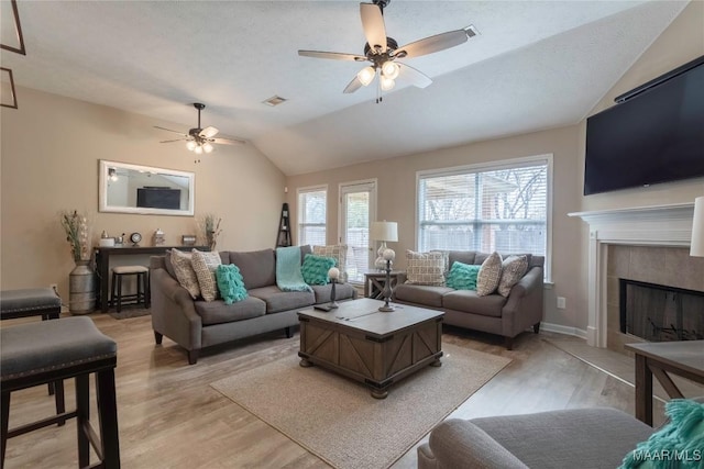 living room featuring lofted ceiling, light hardwood / wood-style flooring, a textured ceiling, a tile fireplace, and ceiling fan