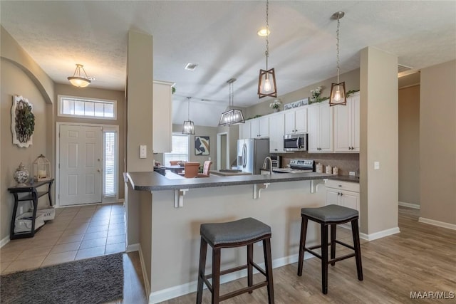 kitchen featuring kitchen peninsula, appliances with stainless steel finishes, white cabinets, a breakfast bar area, and decorative backsplash