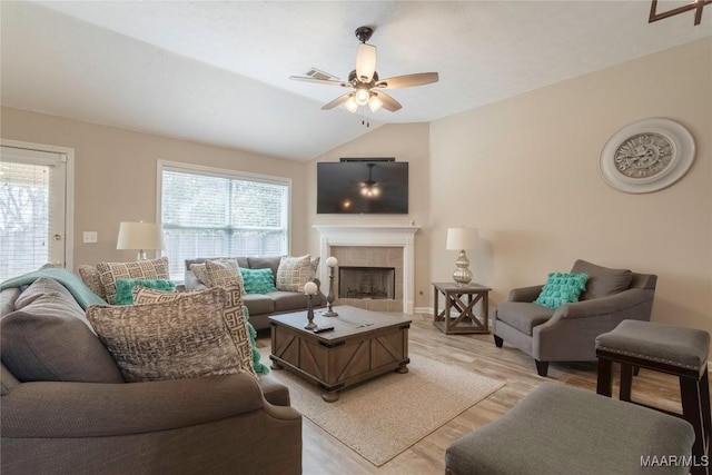 living room with ceiling fan, a tiled fireplace, vaulted ceiling, and light hardwood / wood-style floors